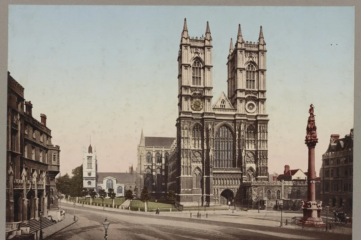 An old colour photograph of the west front of Westminster Abbey, with two stone towers rising behind a street and a tall column.
