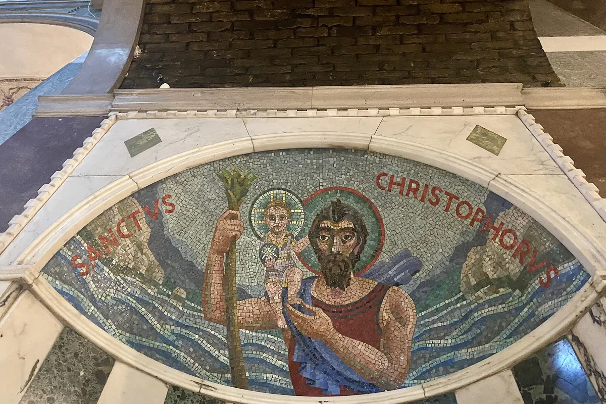 A mosaic of Saint Christopher in a marble frame beneath a vault of bare brick in a side chapel.